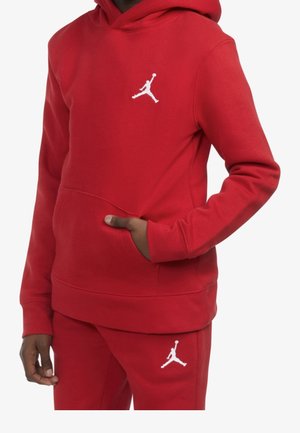 Personne portant un sweat à capuche rouge et un pantalon assorti avec des logos blancs d'un joueur de basket en saut sur la poitrine et la cuisse.