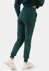 Grüne Jogginghose mit schmalem Schnitt, elastischem Bund, seitlichen Taschen und Bündchen an den Knöcheln, kombiniert mit weißen Sneakern.