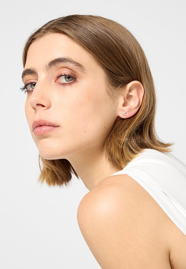Boucles d'oreilles en argent en forme de fleur portées par un modèle. Présentent une forme de fleur délicate, une surface polie et un éclat subtil sur un fond clair.