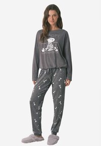 Grå pyjamasset med en långärmad topp med en bild på Snoopy och Woodstock. Byxorna har ett mönster med små Snoopy-figurer och en midja med dragsko.