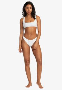 Bílý bikiny set s topem s čtvercovým výstřihem a kalhotkami s nízkým pasem, vyrobený z texturované látky a minimalistického designu.