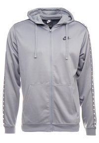Šedá mikina na zip s kapucí a předními kapsami. Obsahuje černé logo a pruhy s textem "NIKE" podél rukávů. Hladký povrch.