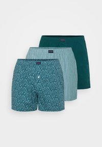 Trois paires de boxers pour hommes : une avec un motif teal, une avec des rayures teal, et une en teal uni. Tous disposent de ceintures élastiques et d'étiquettes en tissu.