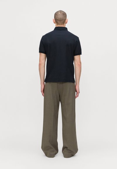 Svart kortärmad polo skjorta med krage, i kombination med vida beige byxor. Tyget verkar slätt med en avslappnad passform.