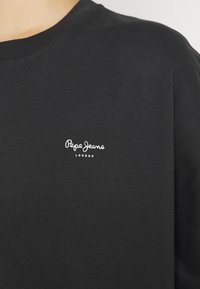 T-shirt nera in cotone a maniche corte; presenta il logo bianco "Pepe Jeans London" sulla parte sinistra del petto. Texture liscia, scollatura classica a girocollo.