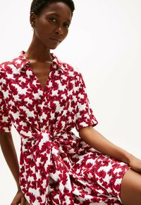 Abito a maniche corte in tessuto bianco decorato con stampa floreale rossa, con colletto e dettaglio a fiocco in vita per un effetto raccolto.