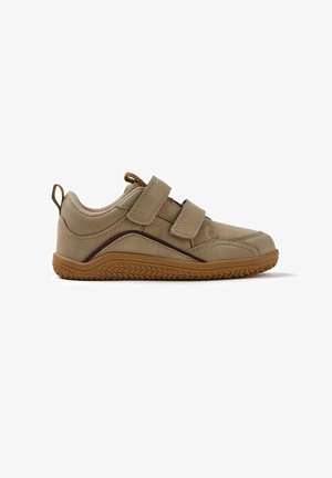 Zapato de cuero beige con un cuello acolchado, doble correa de Velcro y una suela de goma marrón texturizada que presenta un patrón en zigzag.