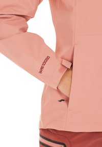 Lys rosa vandtæt jakke med justerbare manchetter, der har "W PRO 10000" branding. Glat tekstur og minimalistiske designelementer.