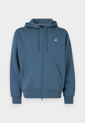 Blauer Zip-Hoodie aus weichem Material, mit Kängurutasche, gerippten Bündchen und einem kleinen weißen Logo auf der Brust.