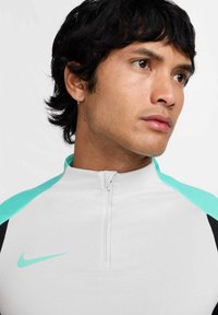 Weißes sportliches Zip-Up-Oberteil mit türkisfarbenen und schwarzen Akzenten. Verfügt über einen hohen Kragen und einen kurzen Reißverschluss vorne. Sportliches Nike-Logo.