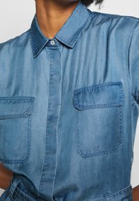 Camicia di jeans di un blu medio con colletto, due tasche sul petto e chiusura con bottoni. Tessuto morbido, finitura leggermente sbiadita con una vestibilità su misura.