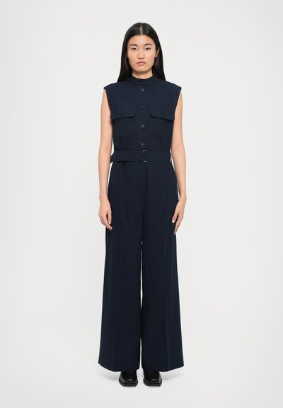 Navy sleeveless jumpsuit with a stand-up collar, button closure, two chest pockets, and a belted waist. Wide-leg design, tailored fit.