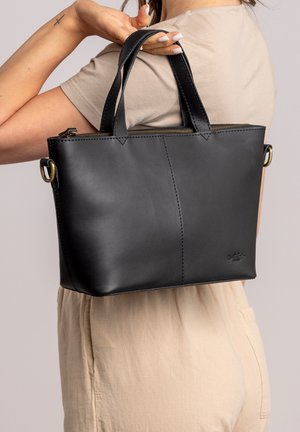Black leather handbag with double handles, zip closure, and gold-tone hardware. Smooth texture and simple geometric design.
