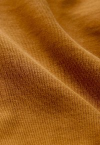 Textured fabric in warm, golden-brown hue with a fine knit pattern, showing subtle ripples and softness in the material.