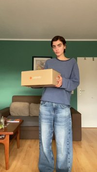 Kartónová krabice s logem Zalando, kterou drží osoba v modro-bíle pruhovaném svetru a světle modrých širokých džínách.