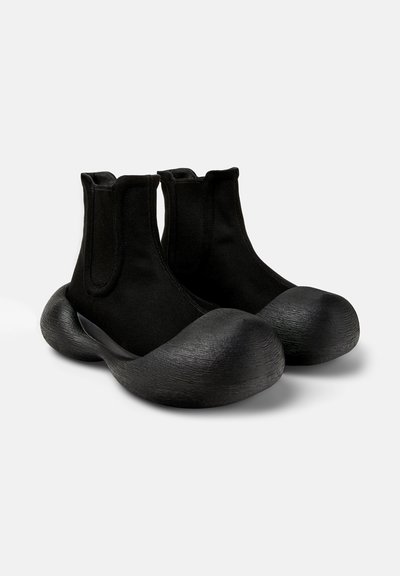 Stivali neri alla caviglia con punta arrotondata e liscia e parte superiore texture, dotati di pannelli laterali elastici per una facile calzata e una suola audace e scultorea.