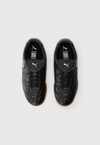 Pair of black Puma soccer shoes with gum soles, laces, and a flap displaying the Puma logo, set against a white background.