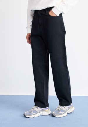 Black denim trousers with a loose fit, featuring a classic five-pocket design, paired with gray and purple athletic shoes.