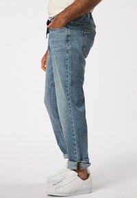 Vaqueros de mezclilla azul claro con corte relajado, cinturilla elástica con cordón y puños enrollados, combinados con zapatillas blancas.