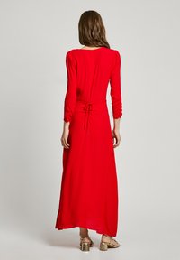 Robe maxi rouge à manches longues avec une taille cintrée, des détails froncés aux manches et un lien dans le dos. Texture lisse.