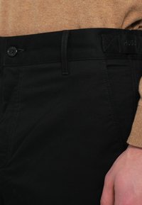 Μαύρο παντελόνι από λείο ύφασμα, με τυπική μέση που κλείνει με κουμπί και λογότυπο HUGO στο πίσω μέρος.