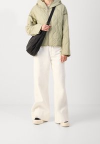 Veste matelassée vert clair avec capuche, associée à un pantalon blanc à jambes larges, et un sac bandoulière noir. Baskets noires et blanches aux pieds.