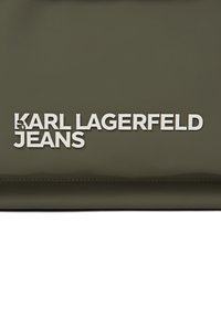 Olíva zöld fényes táska, amelyen fehér "KARL LAGERFELD JEANS" logó van dombornyomva. Simább textúra, varrott szélekkel.
