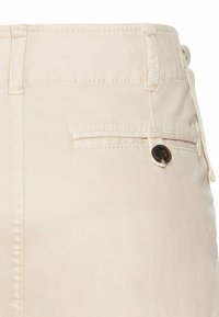 Beige bomuldsbukser med flad front, sømdetaljer og en baglomme med brun knaplukning. Glat tekstur, afslappet design.