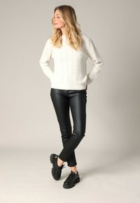 Un pull blanc à côtes associé à des pantalons en faux cuir noir ajustés et des chaussures noires à lacets. Design simple avec des détails texturés.