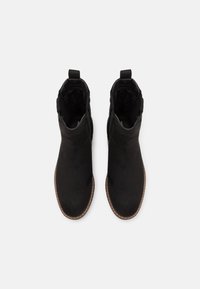 Botas de tobillo negras de material suave, con textura lisa, punta redondeada, diseño de fácil puesta y costuras en contraste en la suela.