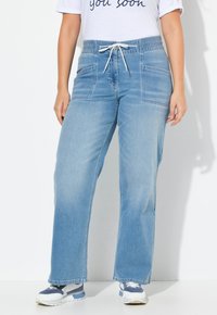 Ljusblå denim-joggers med en avslappnad passform, elastisk midjeband och sidofickor. Stylad med en vit skjorta och sneakers.