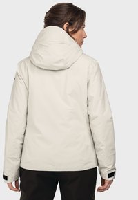 Weiße wasserdichte Jacke mit großer Kapuze, glatter Textur und verstellbaren Manschetten, getragen über dunklen Hosen, mit subtiler Markierung an einem Ärmel.