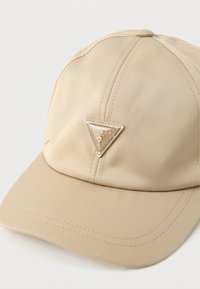 Bēša cepure no gludas auduma ar trīsstūra formas zelta emblemu ar rhinestones, centrēta priekšpusē, ar izšūtu detaļu.