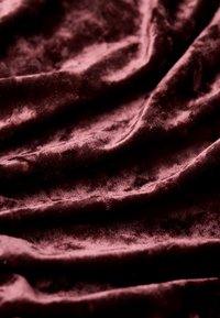 Tissu en velours rouge foncé, doux et froissé, avec des reflets lumineux mettant en valeur sa texture moelleuse et ses plis.