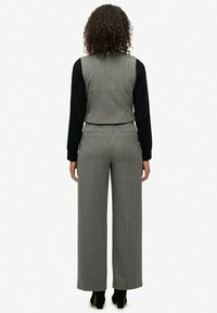 Szary zestaw kamizelki w prążki i szerokich spodni, z gładką czarną bluzką z długim rękawem pod spodem. Gładki materiał i dopasowany krój.