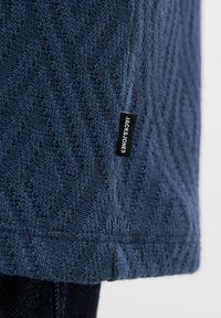 Tamsiai mėlynas megztinis su tekstūruota chevron raštu, su juodu žymekliu, ant šono siuvinėtu „JACK & JONES“. 