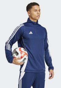Marineblaue sportliche Langarm-Pullover mit weißen Akzenten und Reißverschluss, getragen von einem männlichen Modell, das einen rot-weißen Fußball hält.