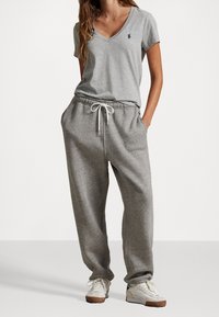 Szary T-shirt z krótkim rękawem i dekoltem w serek, z małym niebieskim logo, zestawiony z szarymi spodniami dresowymi z elastyczną talią i sznurkiem.