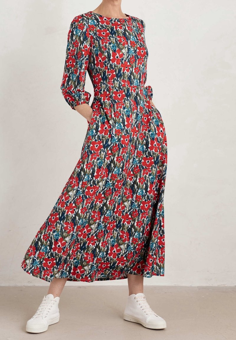 Robe maxi à imprimé floral rouge avec des manches trois-quarts, des poches et un col rond, associée à des baskets montantes blanches.