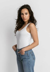 Witte mouwloze tanktop gecombineerd met hoog-waist blauwe spijkerbroek. De stof lijkt zacht, met een getailleerde silhoeet en minimale stiksels.