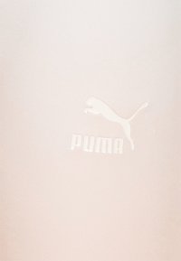 Logo Puma représentant un puma bondissant au-dessus du mot "PUMA" sur un fond beige clair.