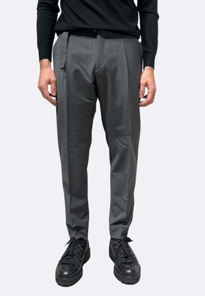 Pantaloni grigi su misura con pieghe, realizzati in tessuto liscio. Indossati con un maglione nero e sneakers nere chunky.