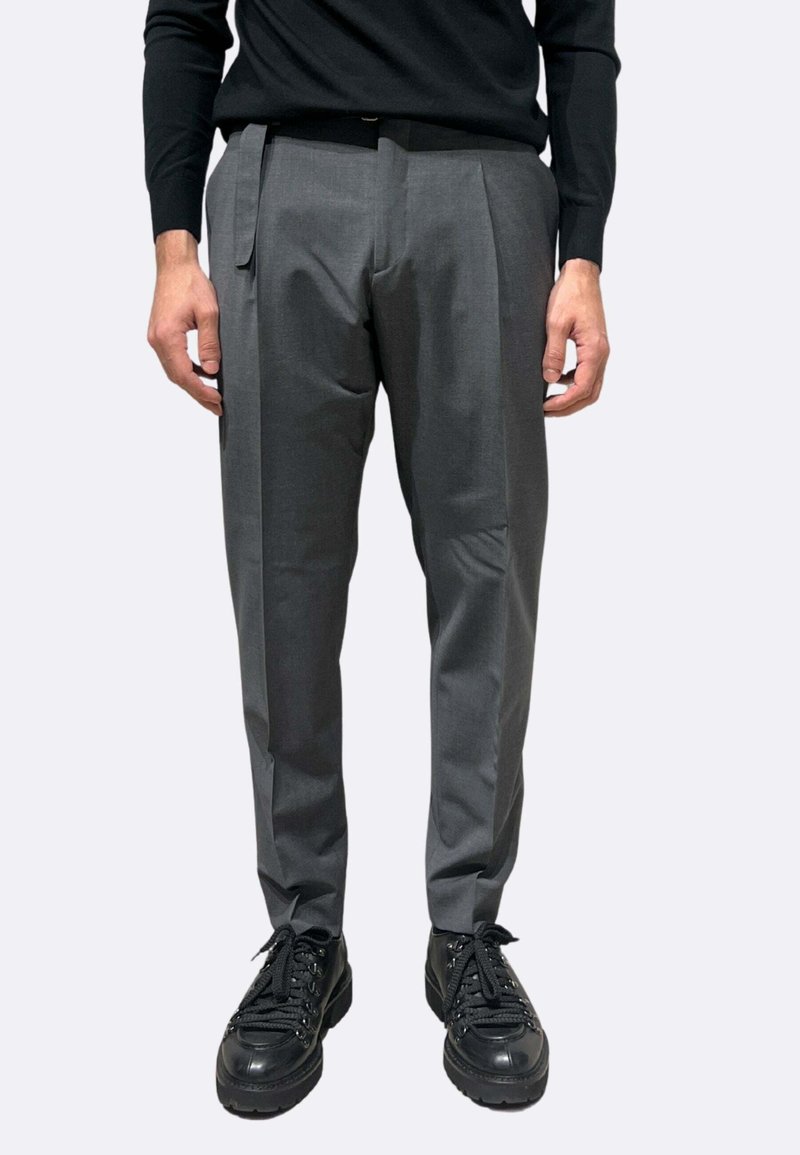 Pantaloni grigi su misura con pieghe, realizzati in tessuto liscio. Indossati con un maglione nero e sneakers nere chunky.
