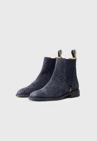 Bottines en daim bleu marine avec des panneaux élastiques sur les côtés, bout arrondi, semelle en caoutchouc noir et accent de tirage à l'arrière pour un enfilage facile.