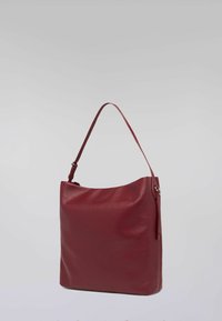 Czerwona skórzana torba na ramię o gładkiej fakturze, prostokątnym kształcie i pojedynczym regulowanym pasku. Charakteryzuje się minimalistycznym designem bez widocznych elementów metalowych.