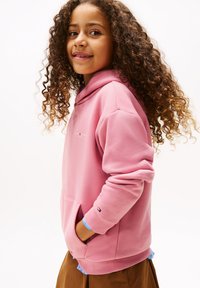 Sweatshirt rosa com capuz, bolso frontal, punhos canelados e detalhe de logo. O tecido parece suave, adequado para uso casual.
