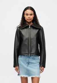 Μαύρο δερμάτινο μπουφάν με ψηλό γιακά, φερμουάρ και μακριά μανίκια. Φορεμένο με ανοιχτό μπλε τζιν φούστα με ξηλωμένη άκρη.