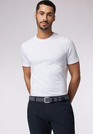 Hvid bomuld t-shirt med korte ærmer, parret med navy-blå bukser og et mønstret bælte med en sølvspænde.