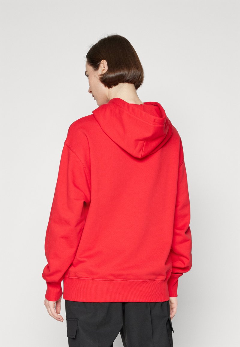 Sweatshirt à capuche rouge avec une coupe décontractée, des poignets et un ourlet côtelés. Caractérisé par une capuche à double couche et une texture douce, porté sur un pantalon cargo noir.
