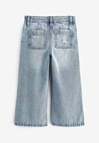 Vaaleansiniset denimgolisthousut, joissa on kaksi takataskua ja röpelöiset helmat. Niissä on kuluneet yksityiskohdat ja klassiset ompelujärjestelyt.